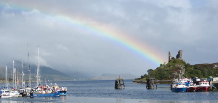 Rainbow at a harbour in Scotland, with a castle ruin in the background