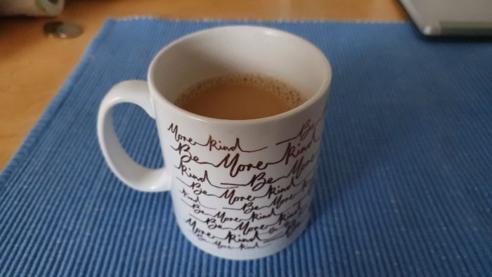 white coffee mug, filled with coffee. Mug has "Be More Kind" written all over it. 