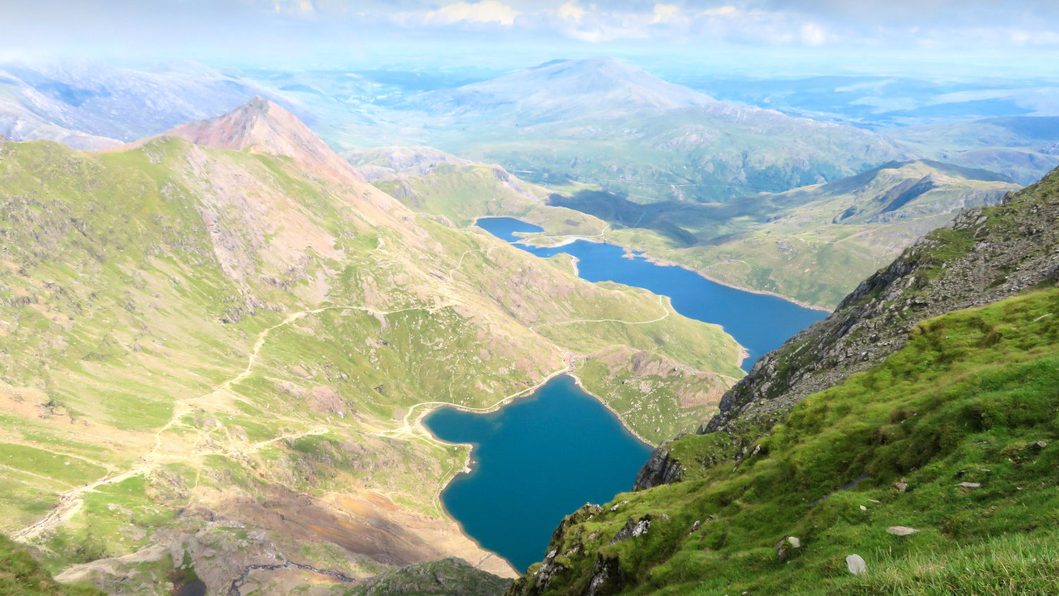 View from up on a mountain on two lakes and green meadows. Cloudy but also sunny sky abvoe