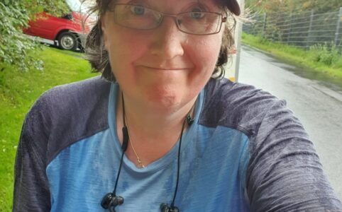 Photo of me with a hat on, wearing a light blue t-shirt. The shirt is soaked from rain