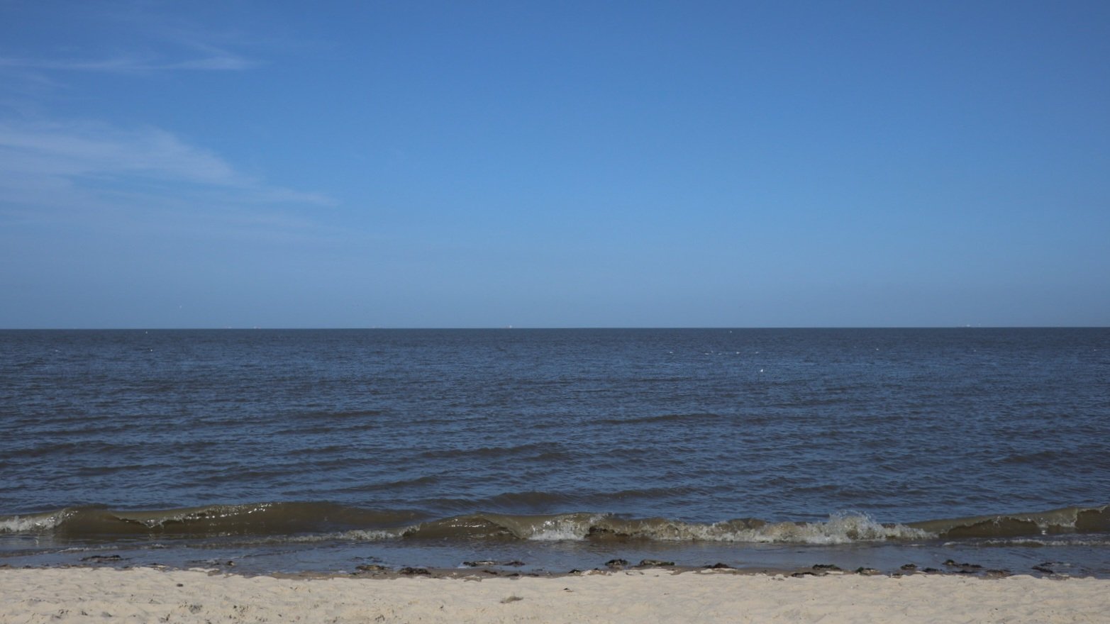 Photo of a rather calm sea. A small stretch of beach in the foreground, small waves and vast sea and blue sky above