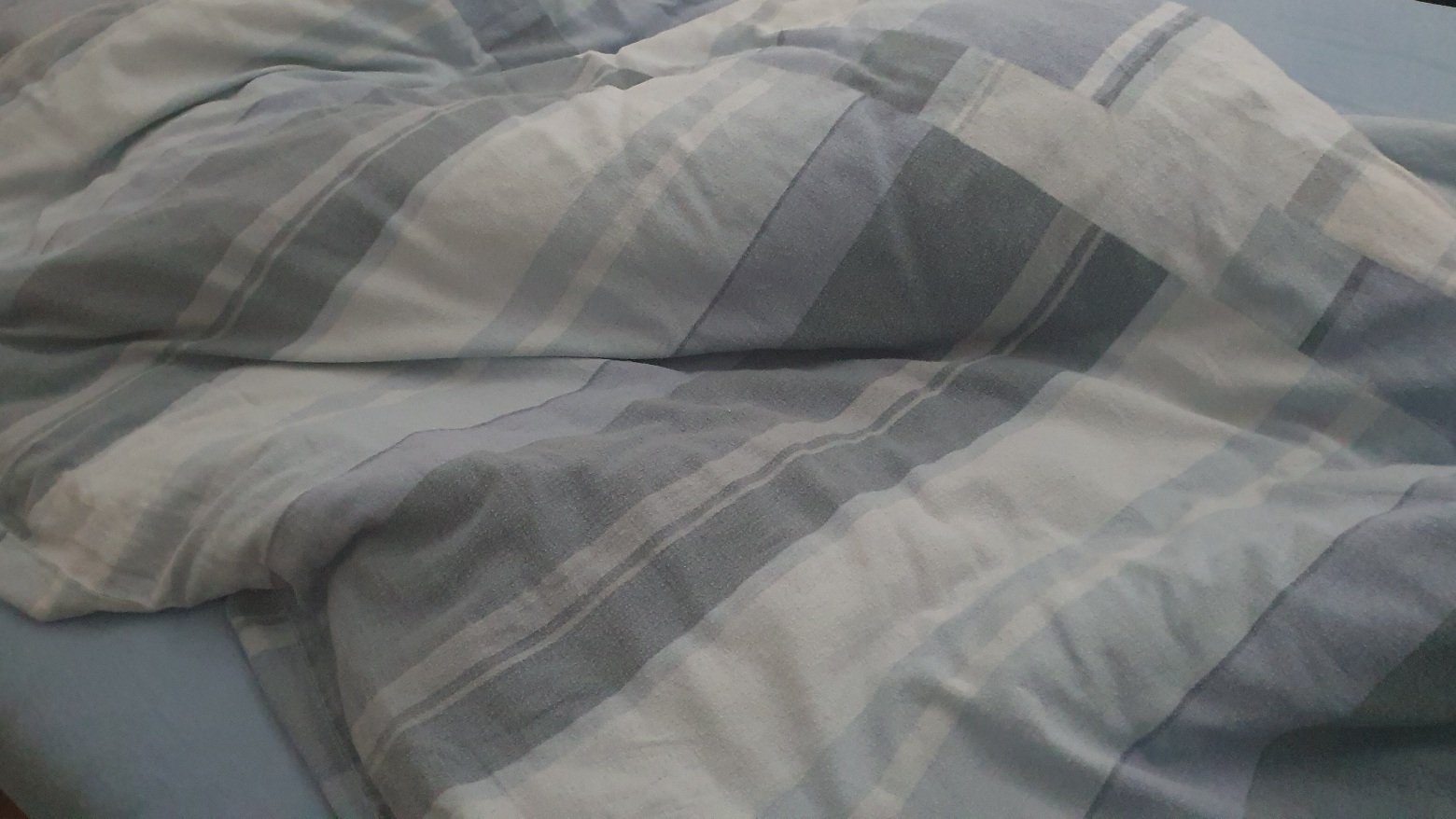 Photo of a duvet on a bed. Duvet cover has stripes in various shades of blue