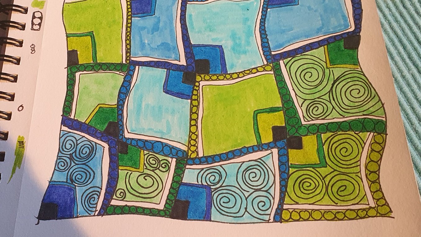 Photo of a half-finished doodling. Wonky squares filled in shades of blue and green. circles drawn on the border lines and spirals in some of the squares