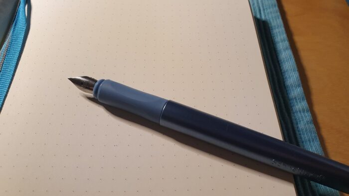 Photo of an uncapped fountain pen laying on blank page of a notebook