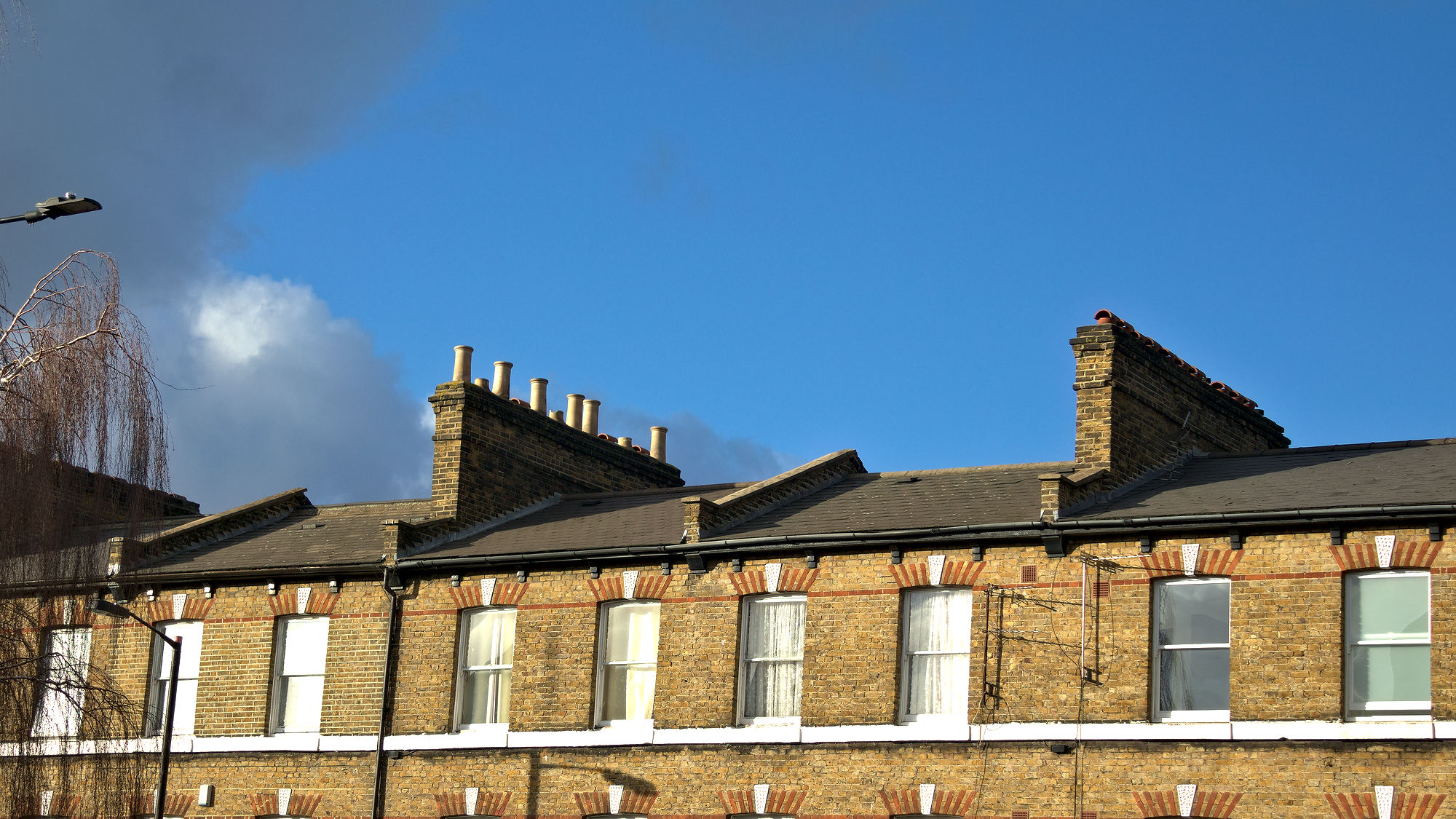 Photo of residential building, top floor and the roof with chimney. Brick walls. Blue sky