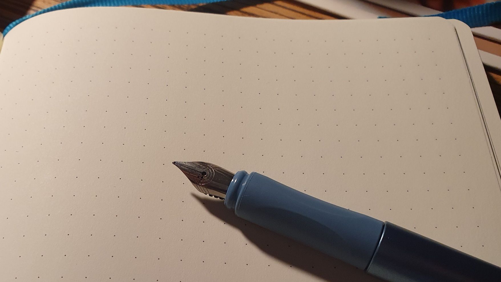 An uncapped fountain pen on an empty page of a dotted page in a journal