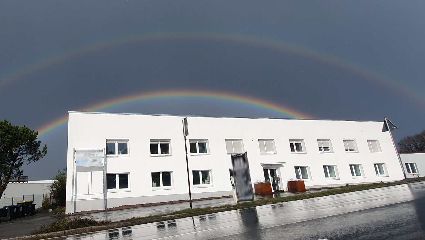 Double rainbow over a two story office building, the street in front is slick from rain