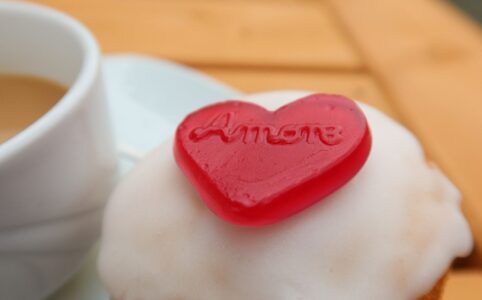 A muffin topped with a red heart saying Amore next to a cup of coffee