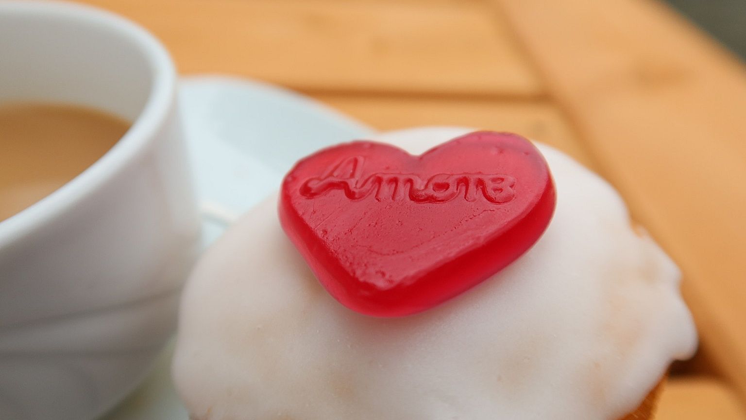 A muffin topped with a red heart saying Amore next to a cup of coffee