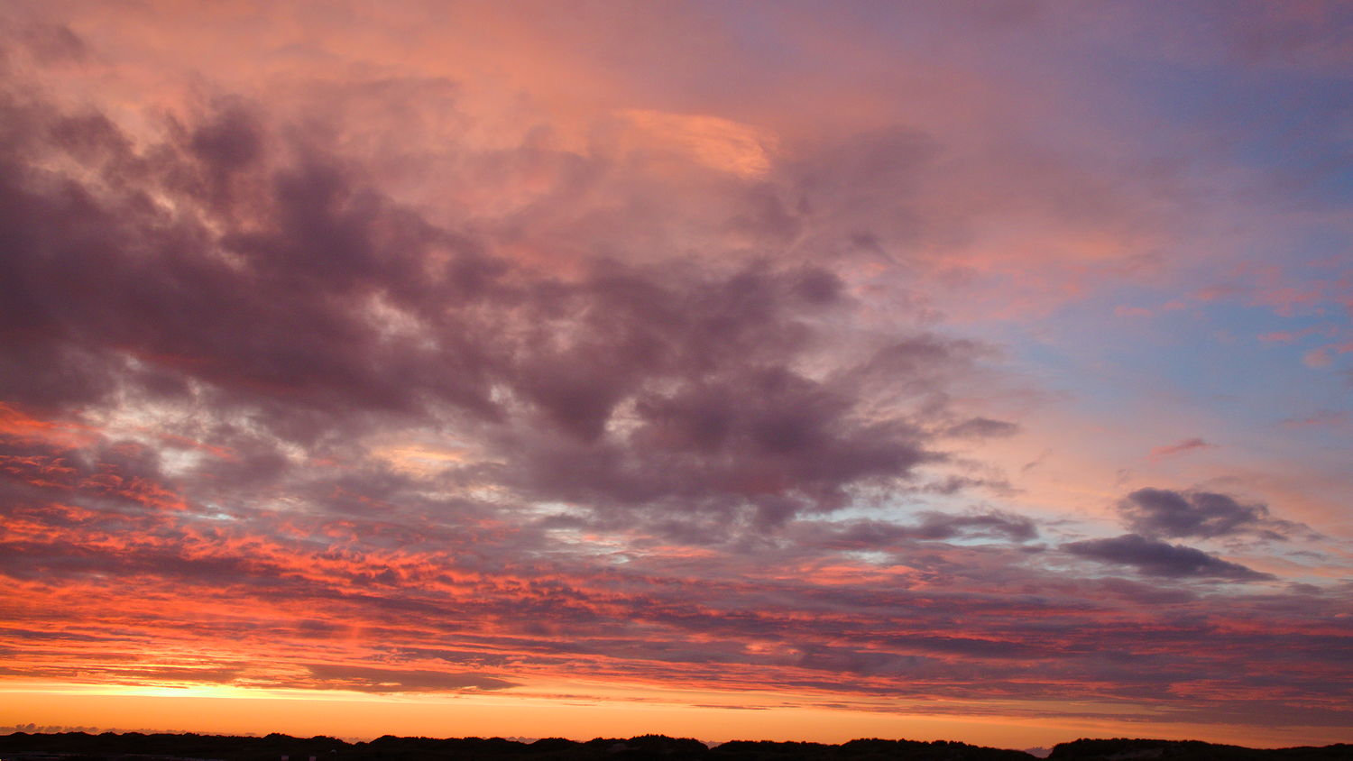 Sky during sunset with the sun setting in the lower left corner and clouds in the upper half of the image