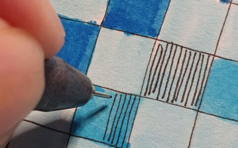 Close up of a few small squares on a page. Coloured in various shades of blue, drawing vertical lines in some of them