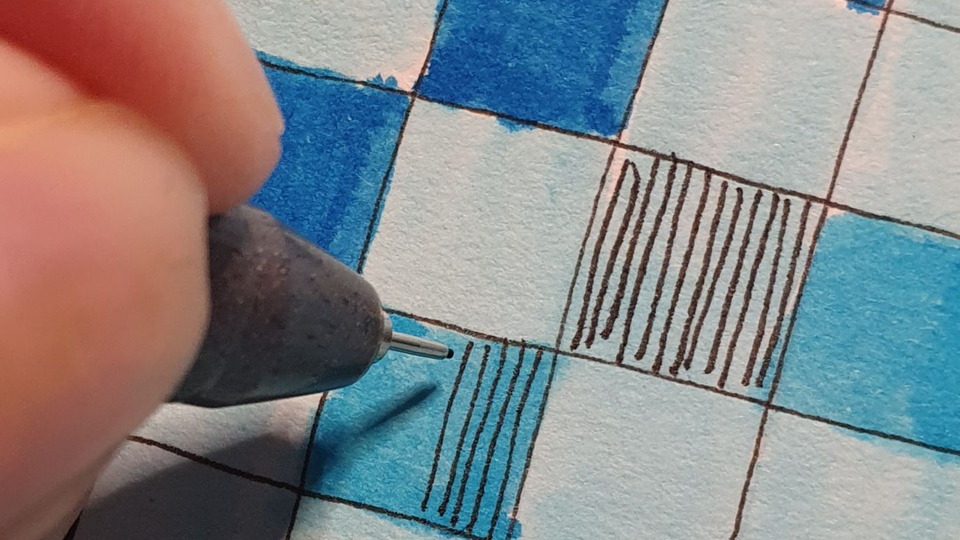 Close up of a few small squares on a page. Coloured in various shades of blue, drawing vertical lines in some of them