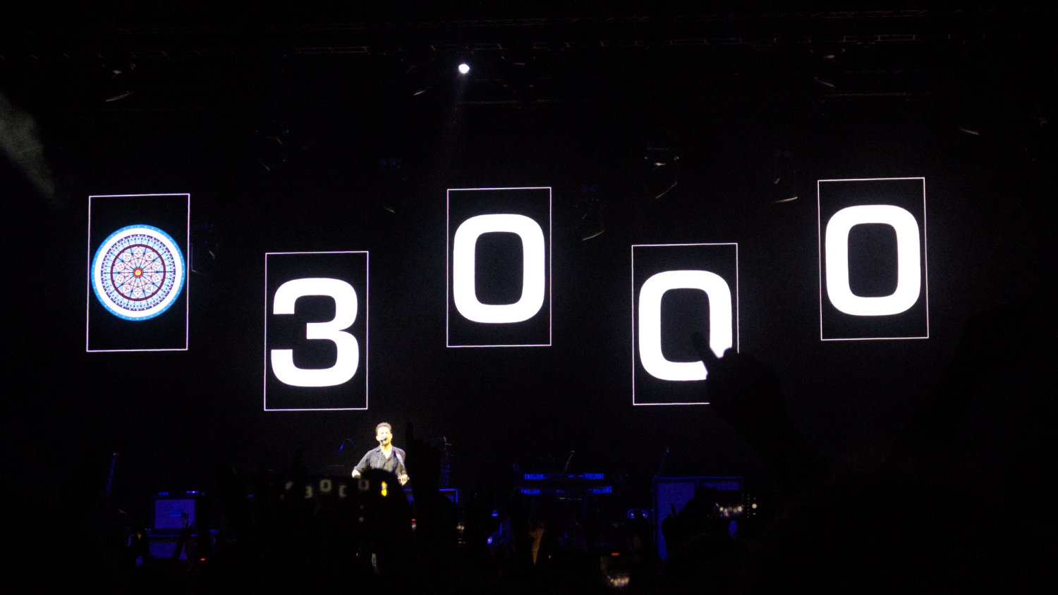 Frank Turner solo on stage with the 3000 on the screen behind him