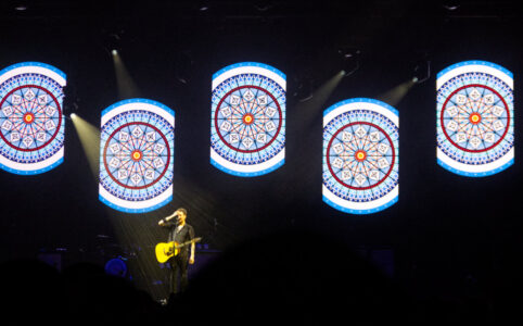 Frank Turner solo on stage with 5 images of the Alexandra Palace stained glass window behind him