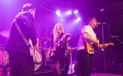 The whole band plus additional guitarist on stage, Katie smiling broadly