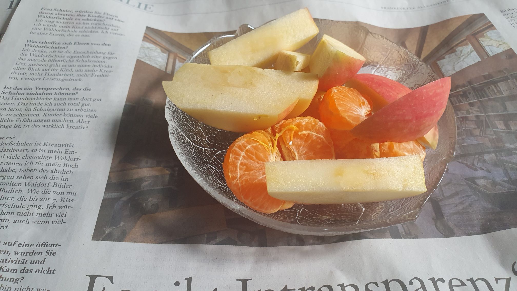 Apple slices and a mandarin in a glas dish on a stack of newspaper